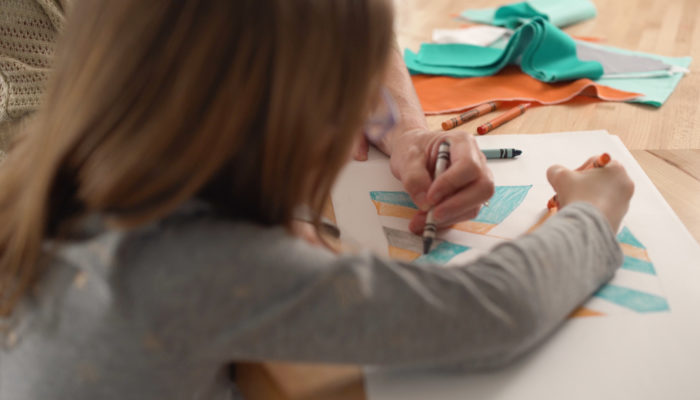 A girl coloring a quilt design on a piece of paper with crayon.